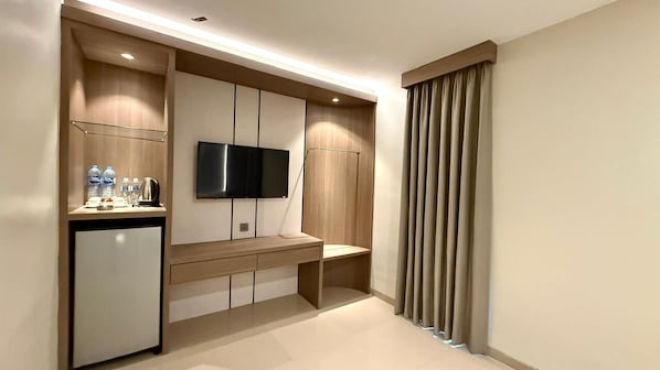 Una habitación de hotel moderna con televisión de pantalla plana en la pared, una pequeña kitchenette con refrigerador y una zona de estar con un banco.