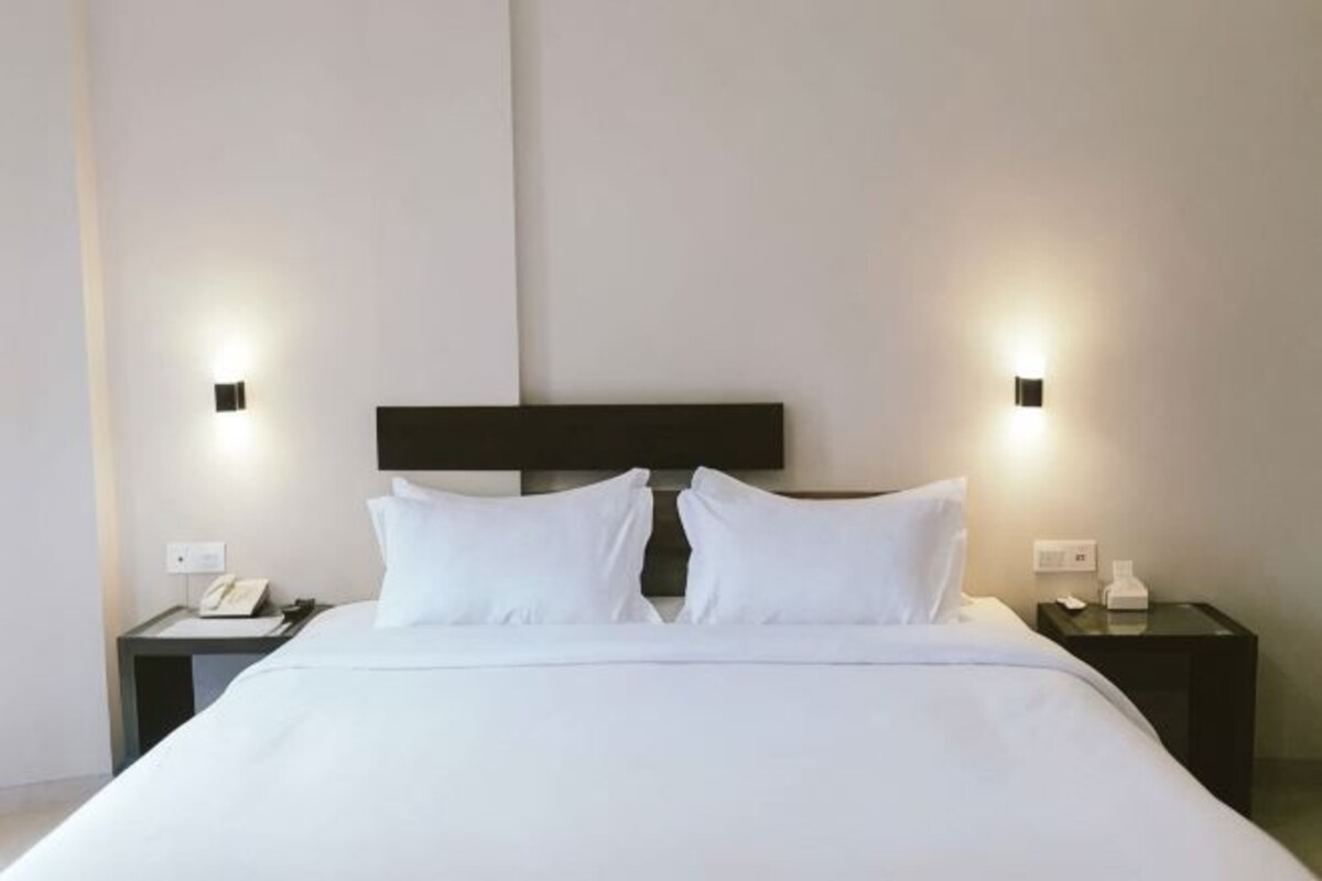 A hotel room with a large bed, two bedside tables, and wall-mounted lights.