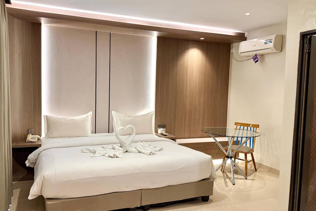 A modern hotel room with a large bed, a glass table, and a chair.