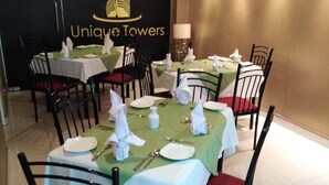 A dining area with tables set for four, each with white tablecloths, red cushioned chairs, and neatly arranged cutlery and plates. - Deluxe 4BR Penthouse By Unique Towers (Colombo)