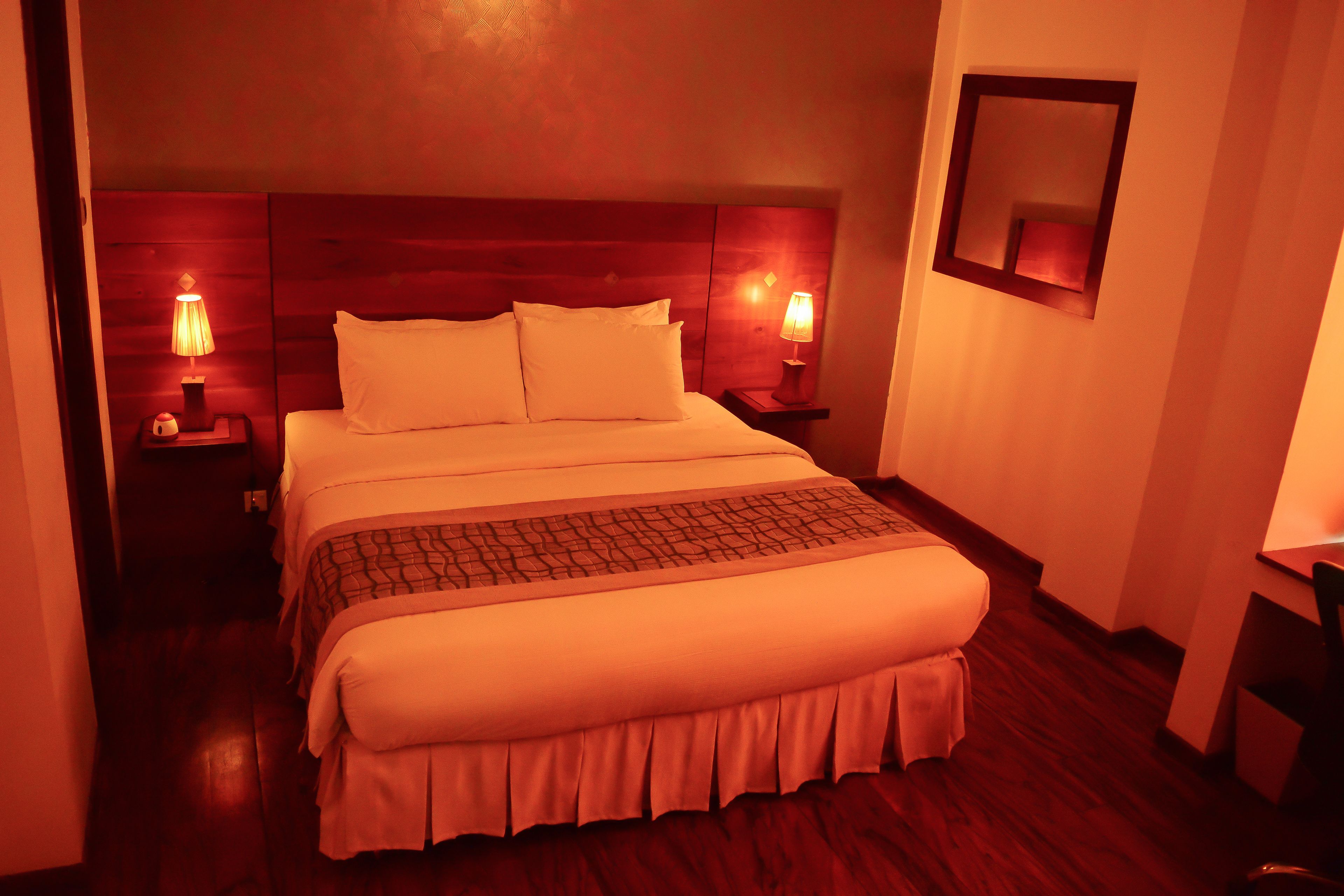 A neatly made bed with a wooden headboard, two bedside lamps, and a mirror on the wall.