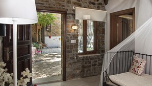 A rustic stone interior with a bed, a lamp, and a view of the courtyard. - The Castle (Gökçeada)