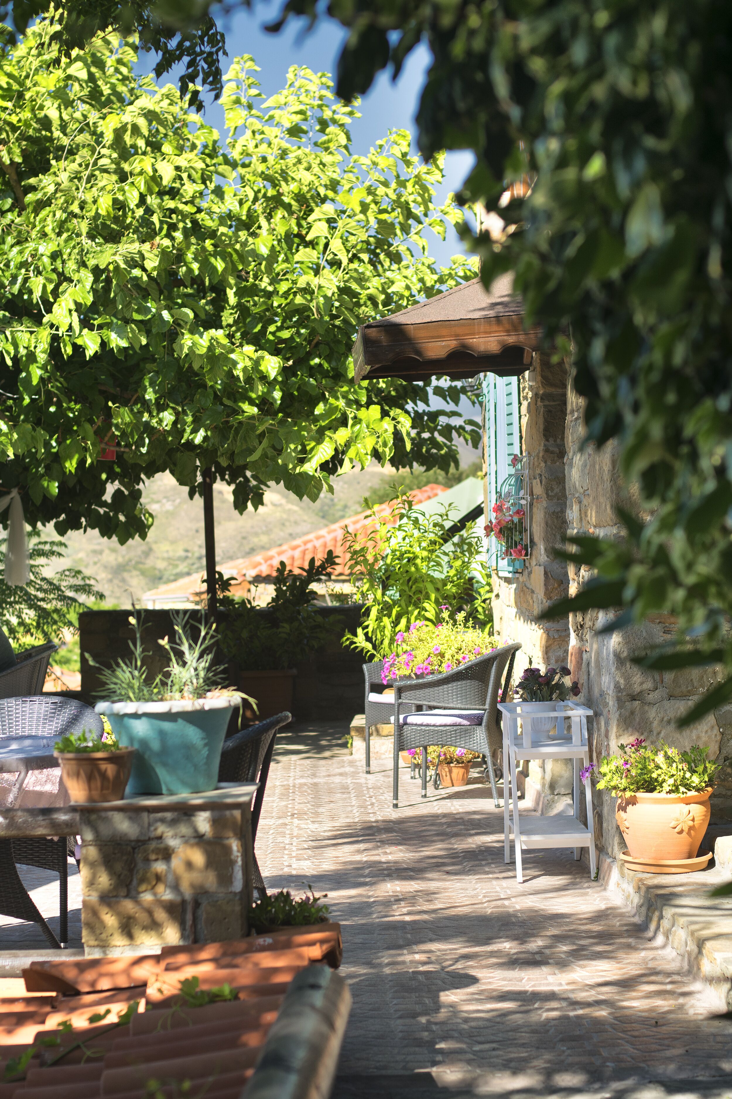 A stone-paved outdoor seating area with wicker furniture, potted plants, and a view of a mountain.