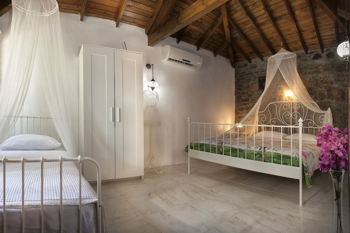 A bedroom with two beds, one with a canopy and one without, a wardrobe, and a stone wall.