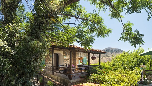 A stone building with a covered patio, surrounded by lush greenery and terracotta roof tiles. - The Castle (Gökçeada)
