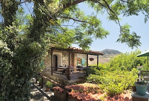 A stone building with a covered patio, surrounded by lush greenery and terracotta roof tiles. - The Castle (Gökçeada)