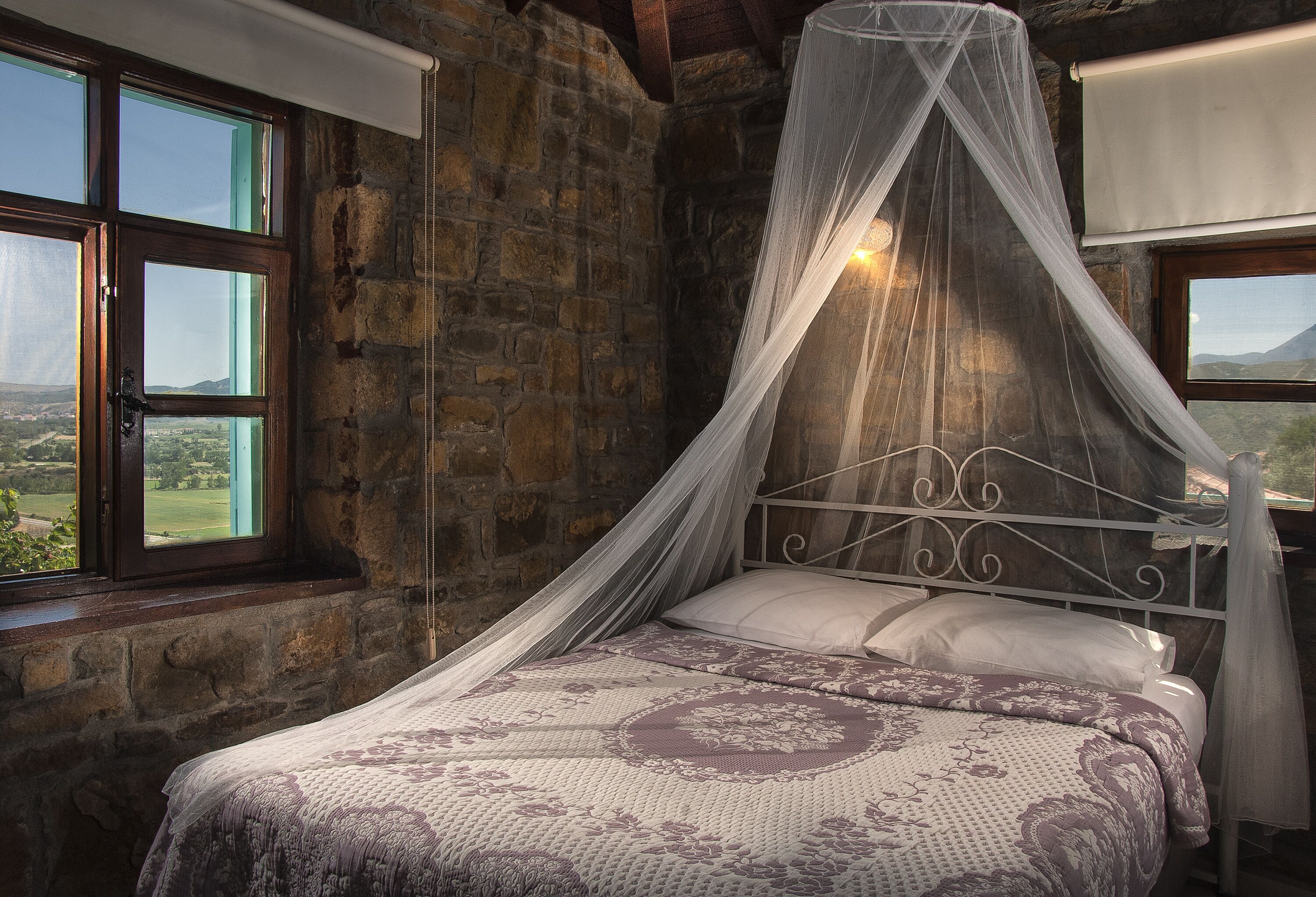 A bed with a canopy in a stone-walled room with large windows.