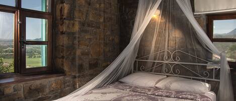 A bed with a canopy in a stone-walled room with large windows.
