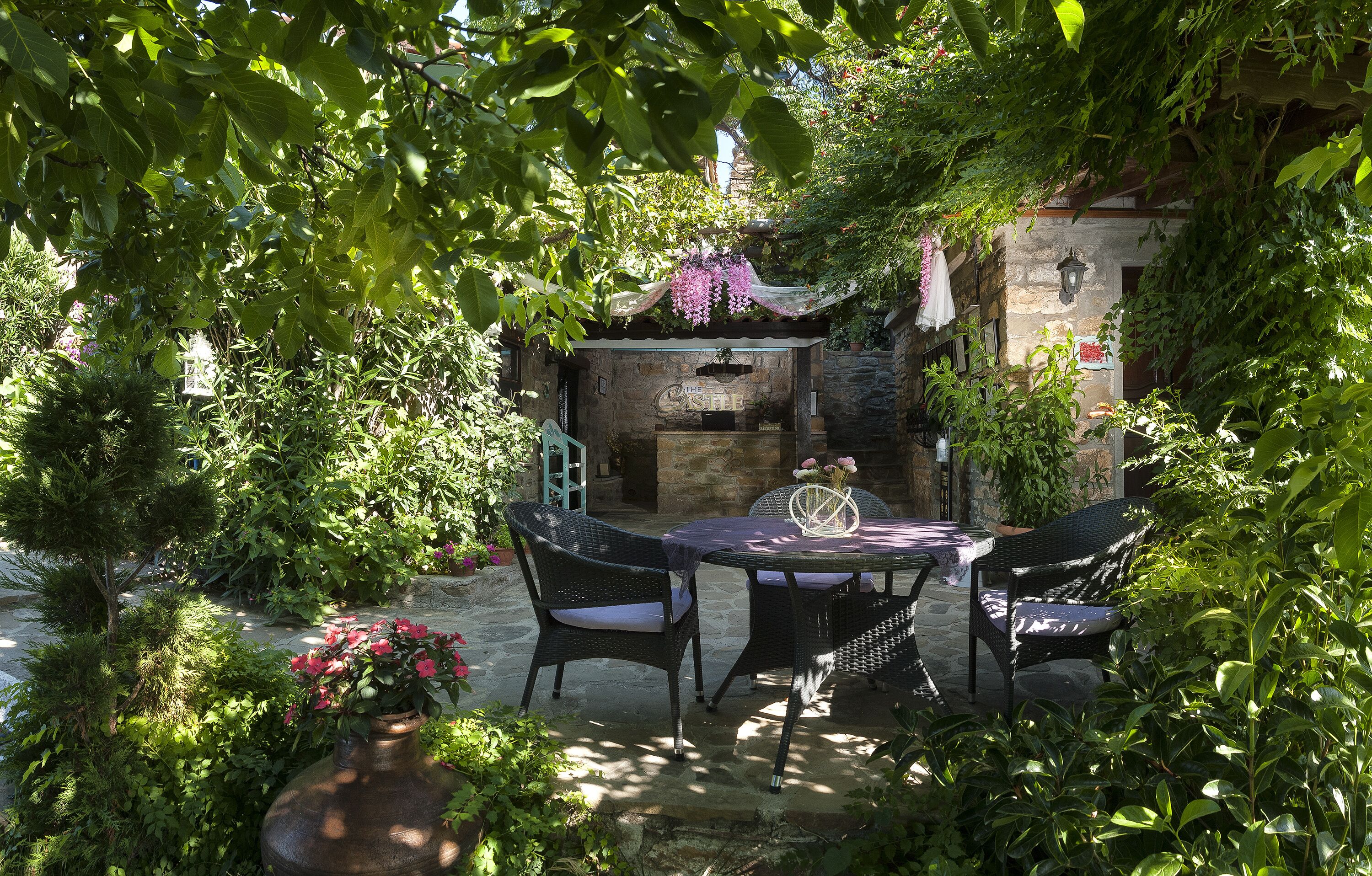 Un patio al aire libre con muebles de mimbre, pared de piedra y abundante vegetación.