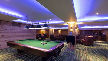 A pool table in a room with wooden walls, a bar area, and seating.