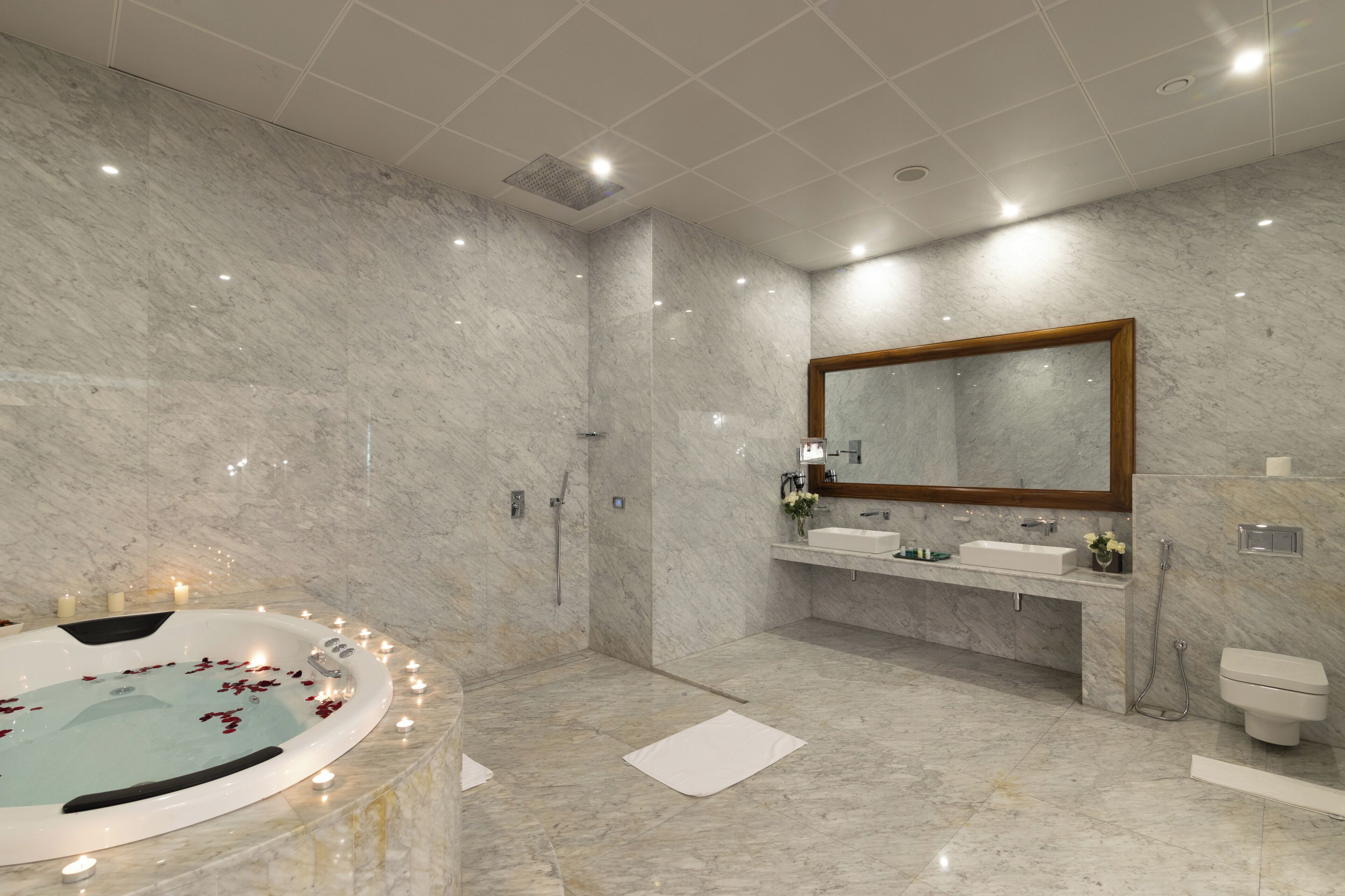 A modern bathroom with a marble floor, a freestanding bathtub, a large mirror, and a vanity with a sink and mirror.