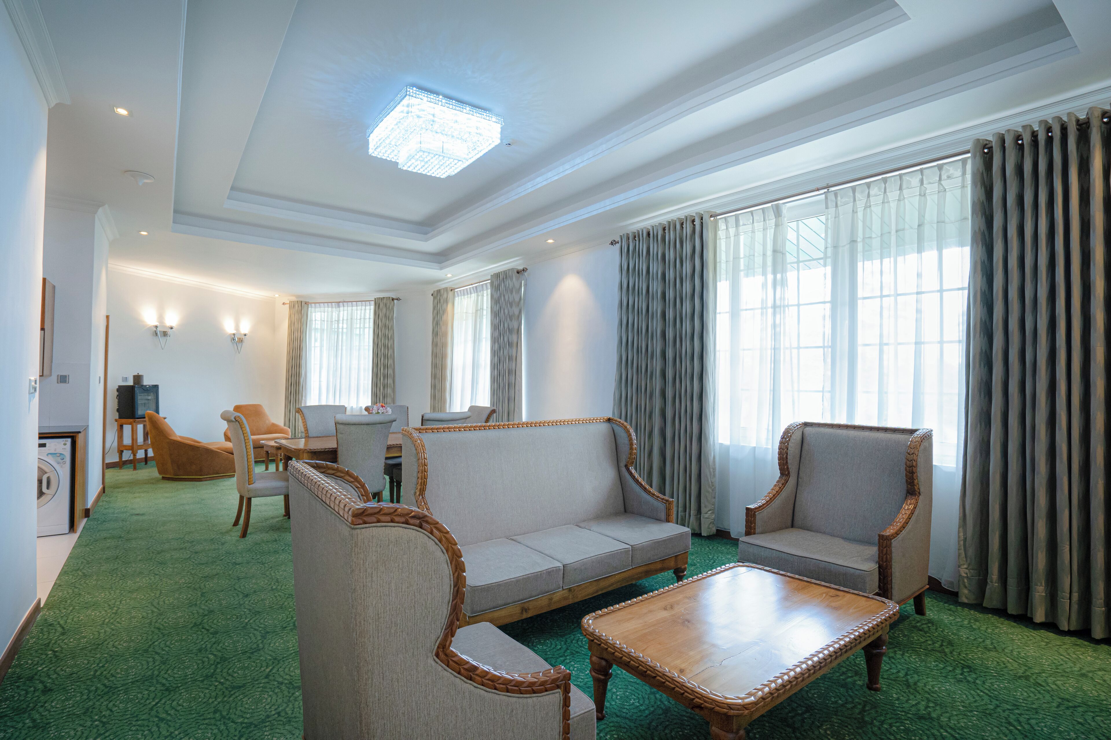 A hotel room with a green carpet, a sofa, two armchairs, a wooden coffee table, and a television in the corner.