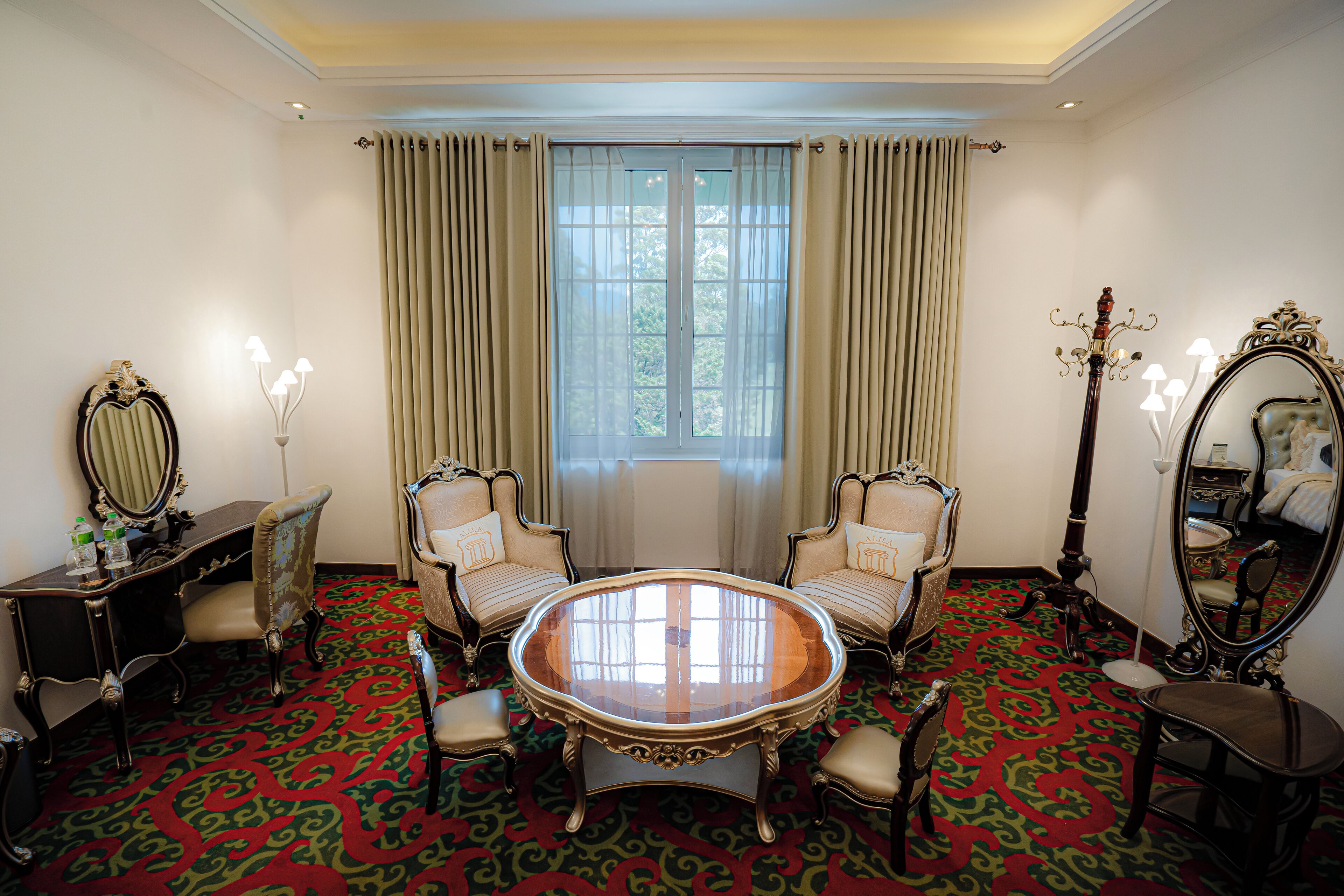 A room with a round table, two chairs, a mirror, and a desk with a lamp.