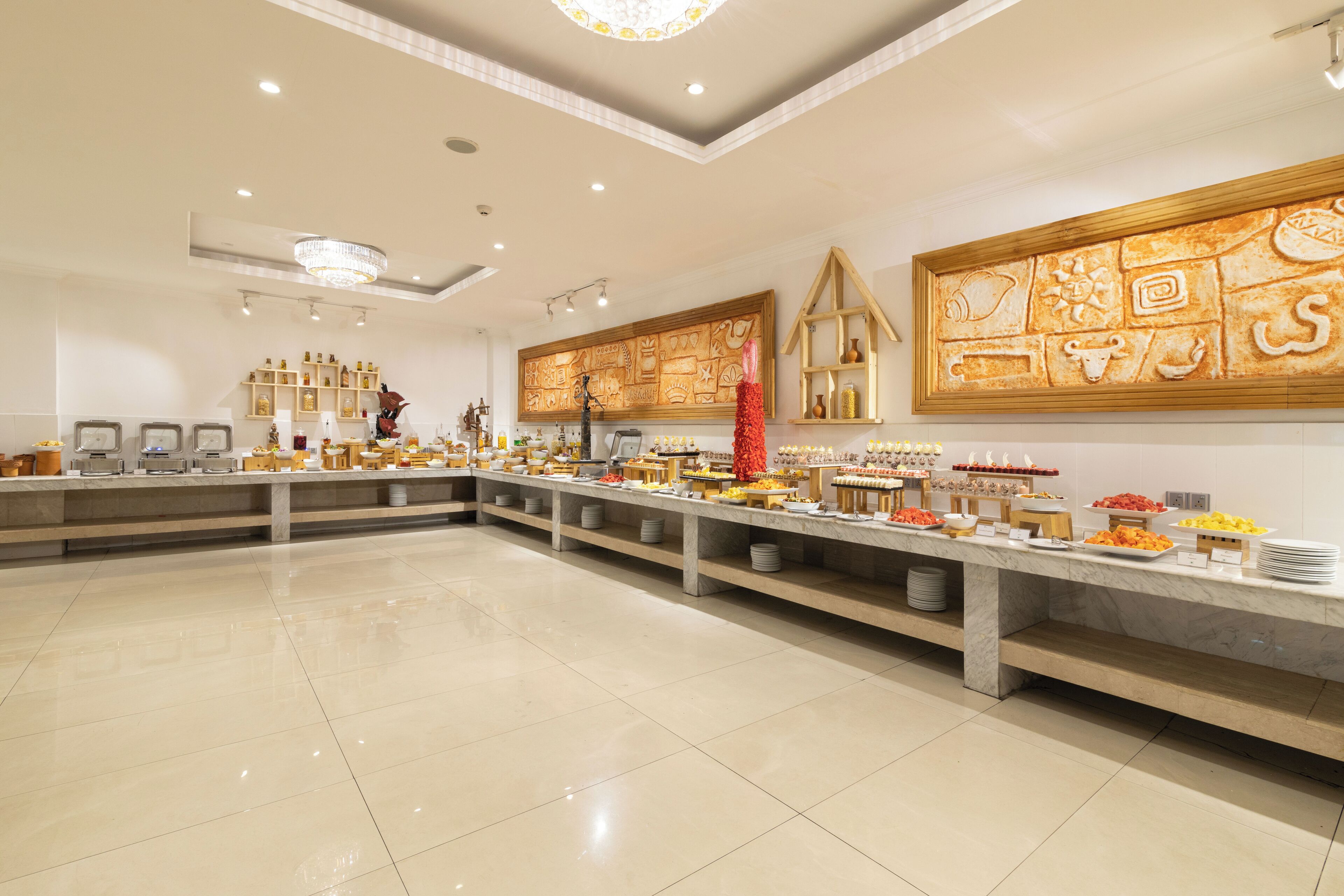 Un área de buffet con una encimera de mármol, diferentes opciones de comida y una pared decorativa con motivos culturales.