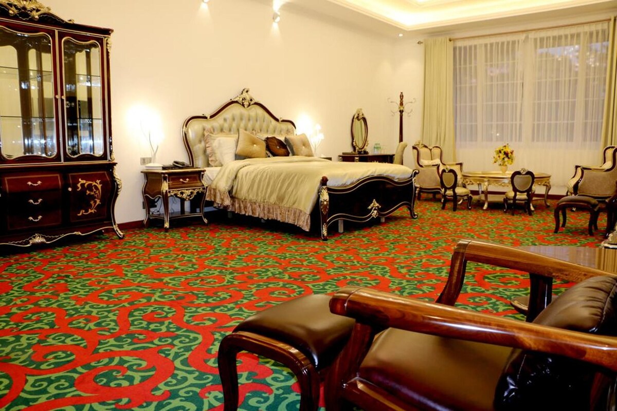 A bedroom with a large bed, a wooden cabinet, a table with chairs, and a window with curtains.
