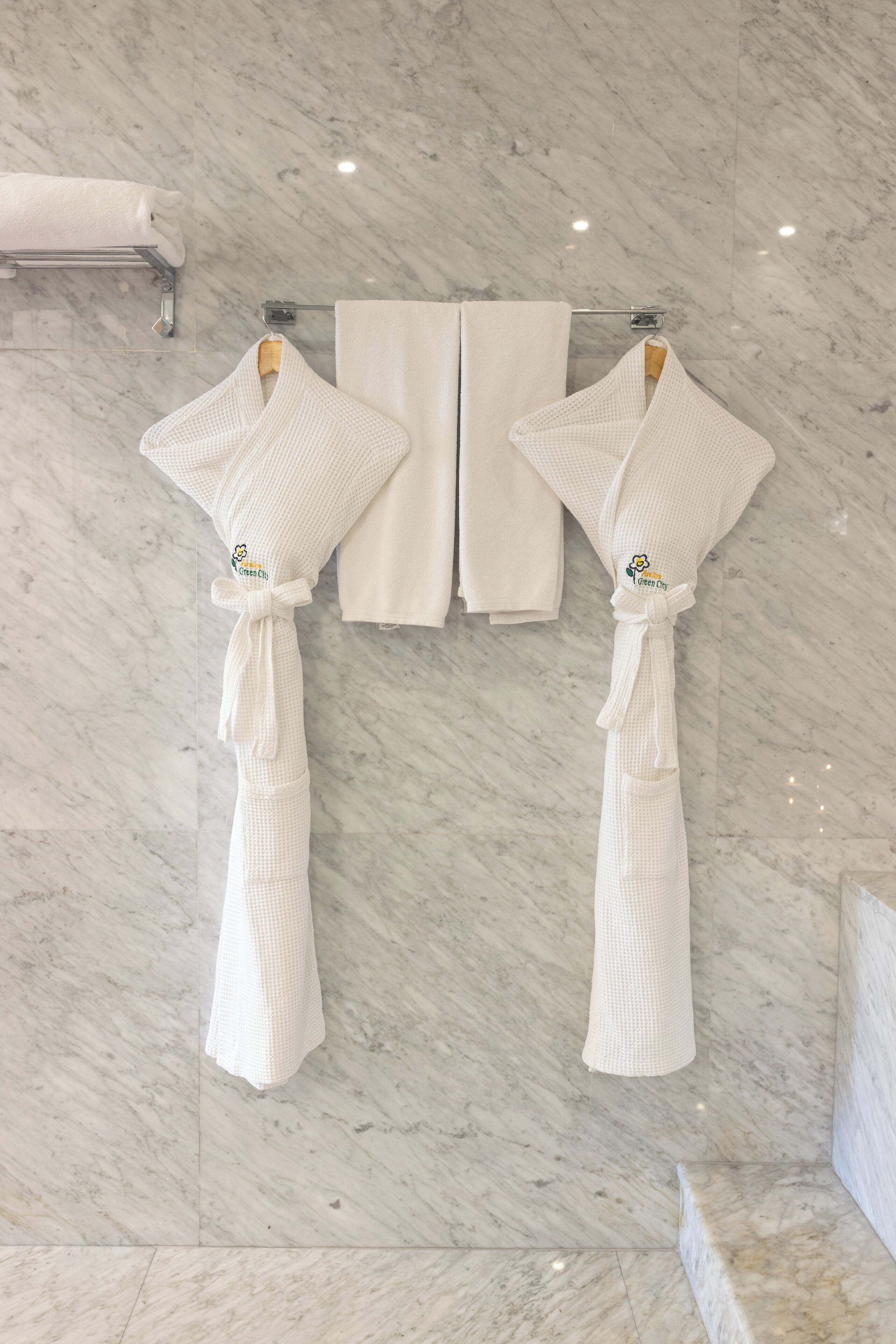 Two white robes hanging on a rack in a bathroom with a marble floor.