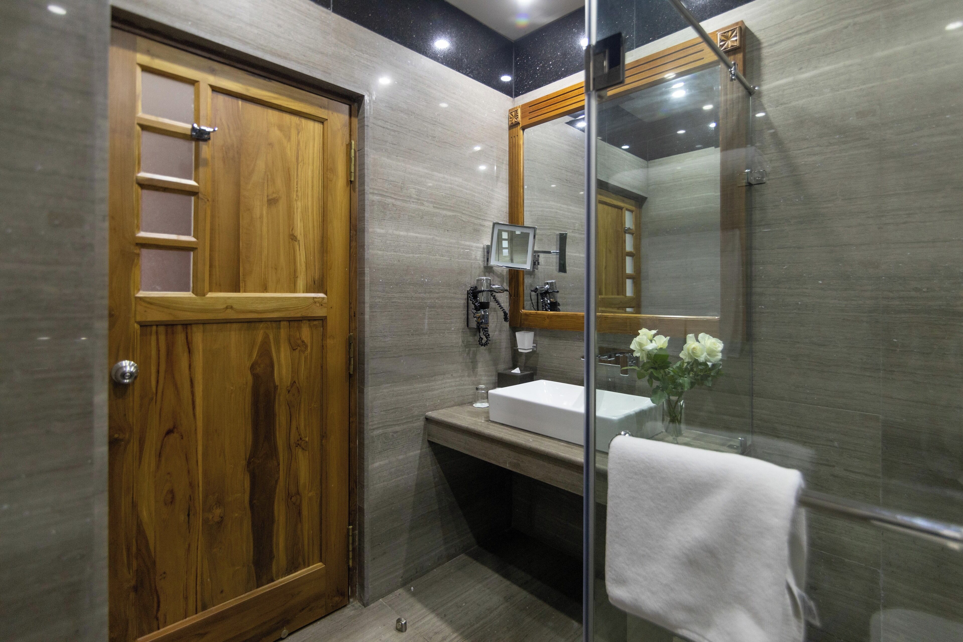 Un baño moderno con puerta de madera, cabina de ducha de vidrio y lavamanos blanco.
