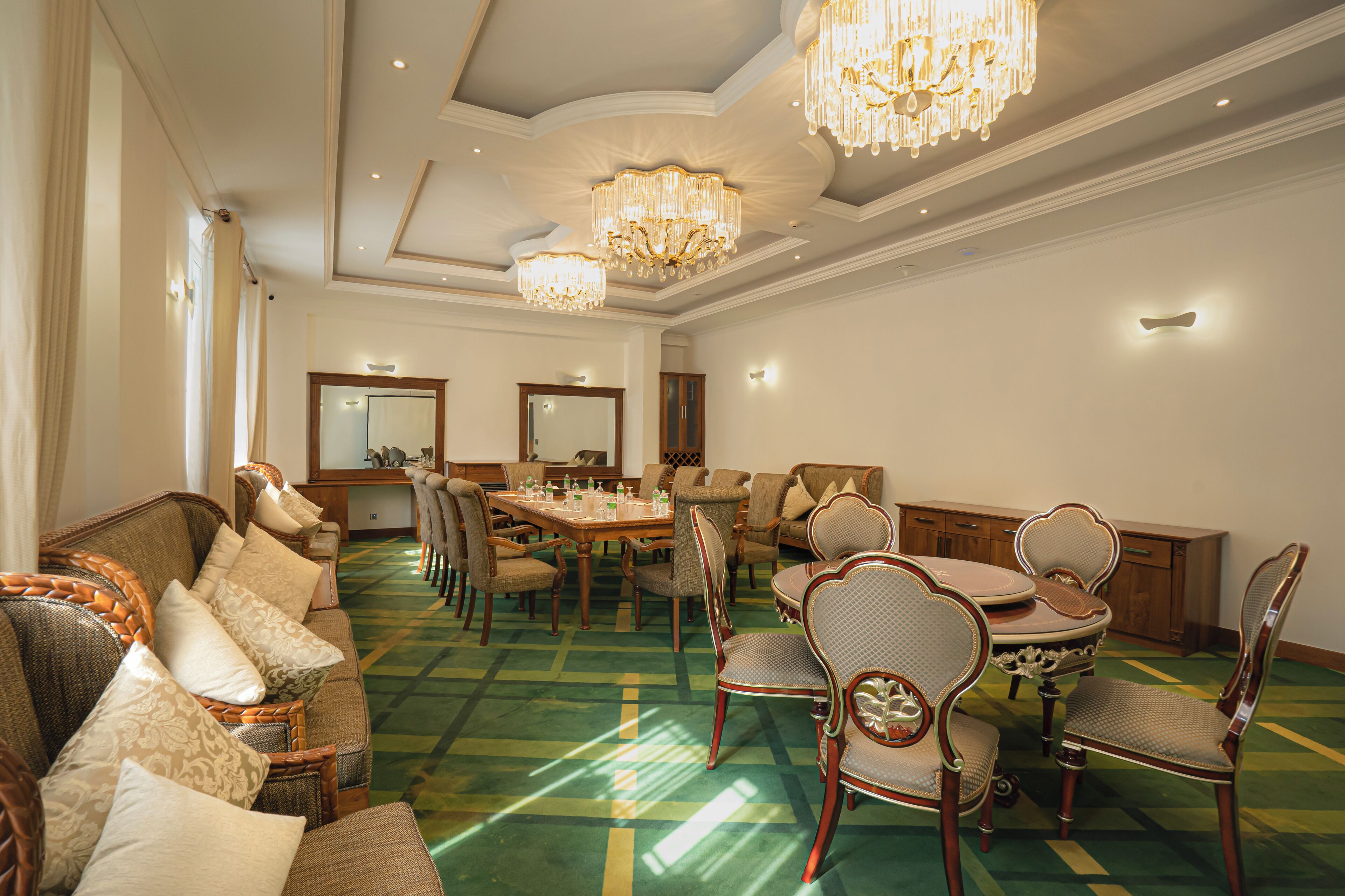 A spacious room with a green patterned carpet, a dining area with a wooden table and chairs, and a seating area with a sofa and armchairs.
