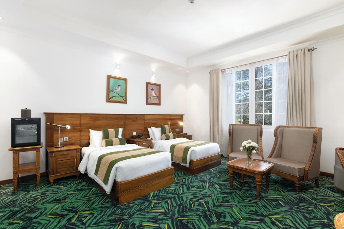 Une chambre d’hôtel avec deux lits, une télévision, un bureau agrémenté d’un vase de fleurs et une fenêtre avec des rideaux.