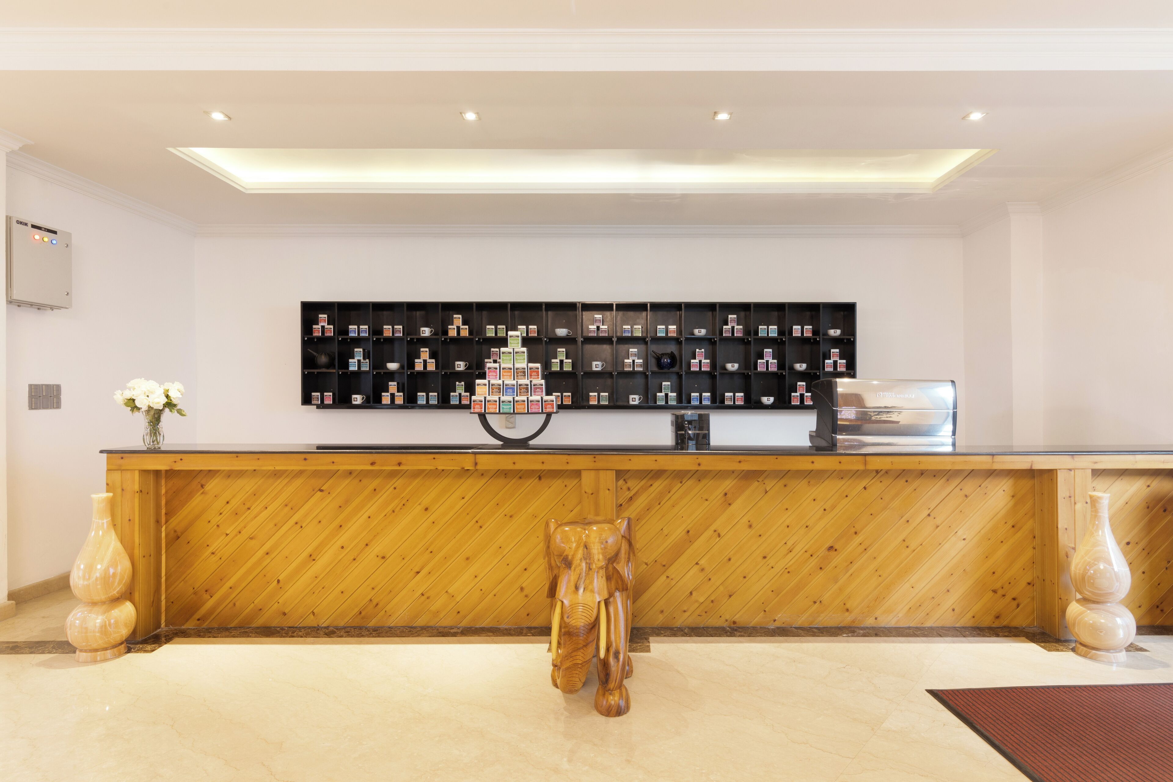 A reception desk with a wooden finish, a black shelf with various items, and a decorative elephant sculpture.