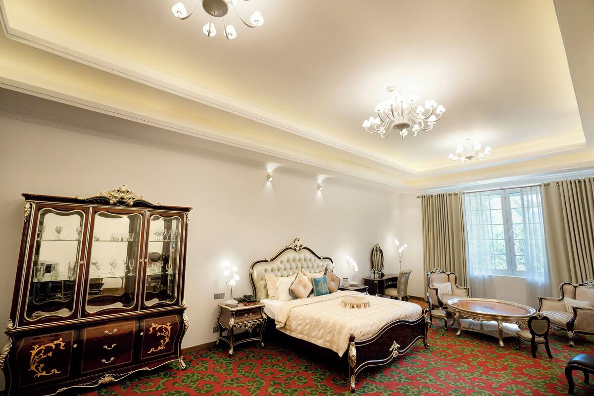 Une chambre à coucher avec un grand lit, une commode, un lustre et une fenêtre avec des rideaux.