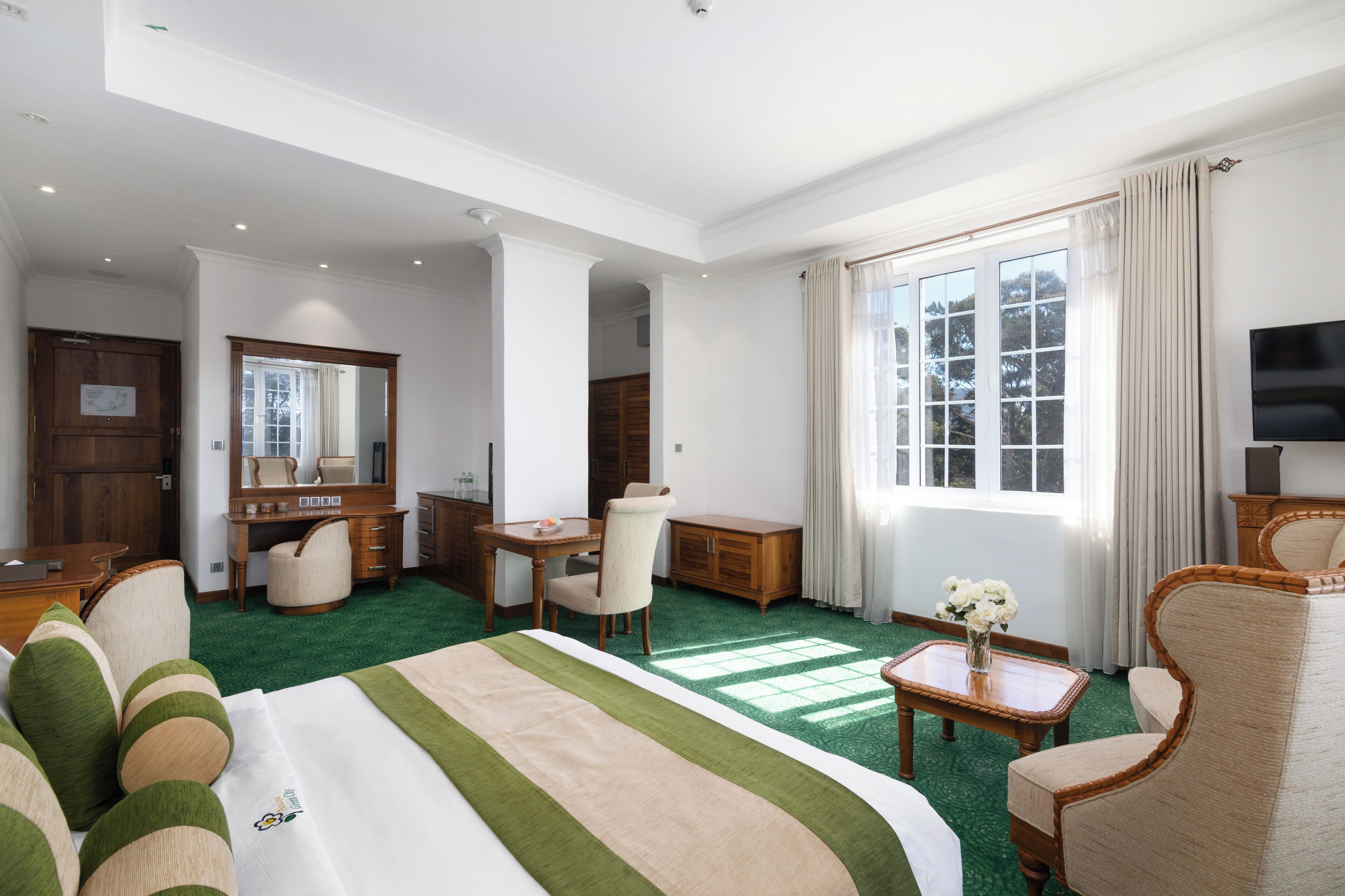 A hotel room with a large bed, a desk, a chair, a television, and a window with curtains.