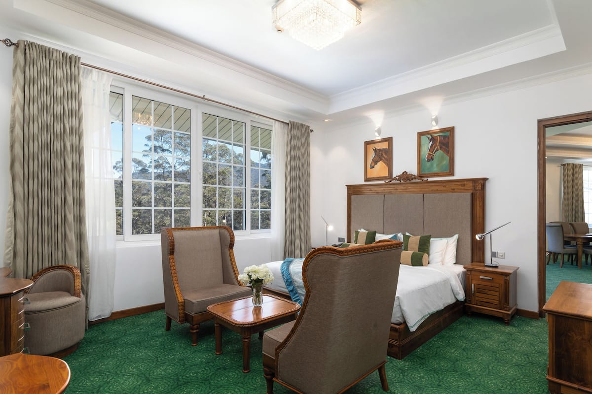 Une chambre d’hôtel avec un grand lit, deux fauteuils, une table de chevet en bois, un bureau et une table à manger.