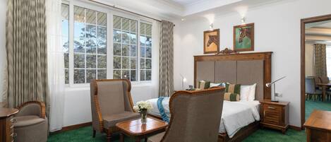 A hotel room with a large bed, two armchairs, a wooden nightstand, a desk, and a dining table.