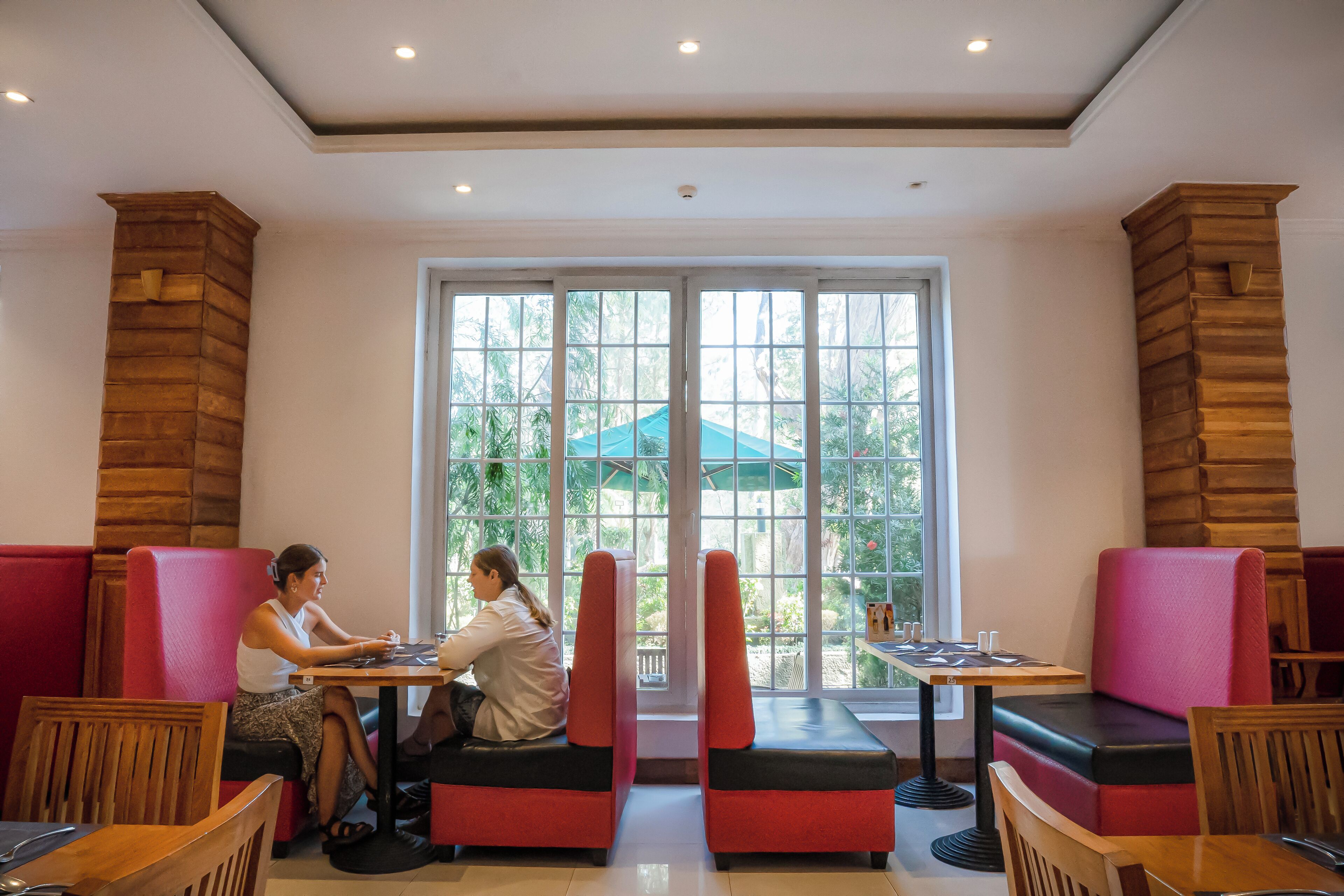 A restaurant with red and black cushioned booths, wooden pillars, and large windows with a view of greenery outside.