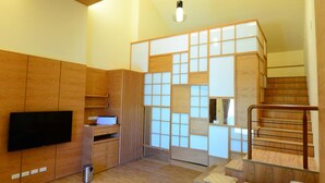 Una sala de estar moderna con suelo de madera, un sofá, un televisor, una escalera y una zona de cocina.