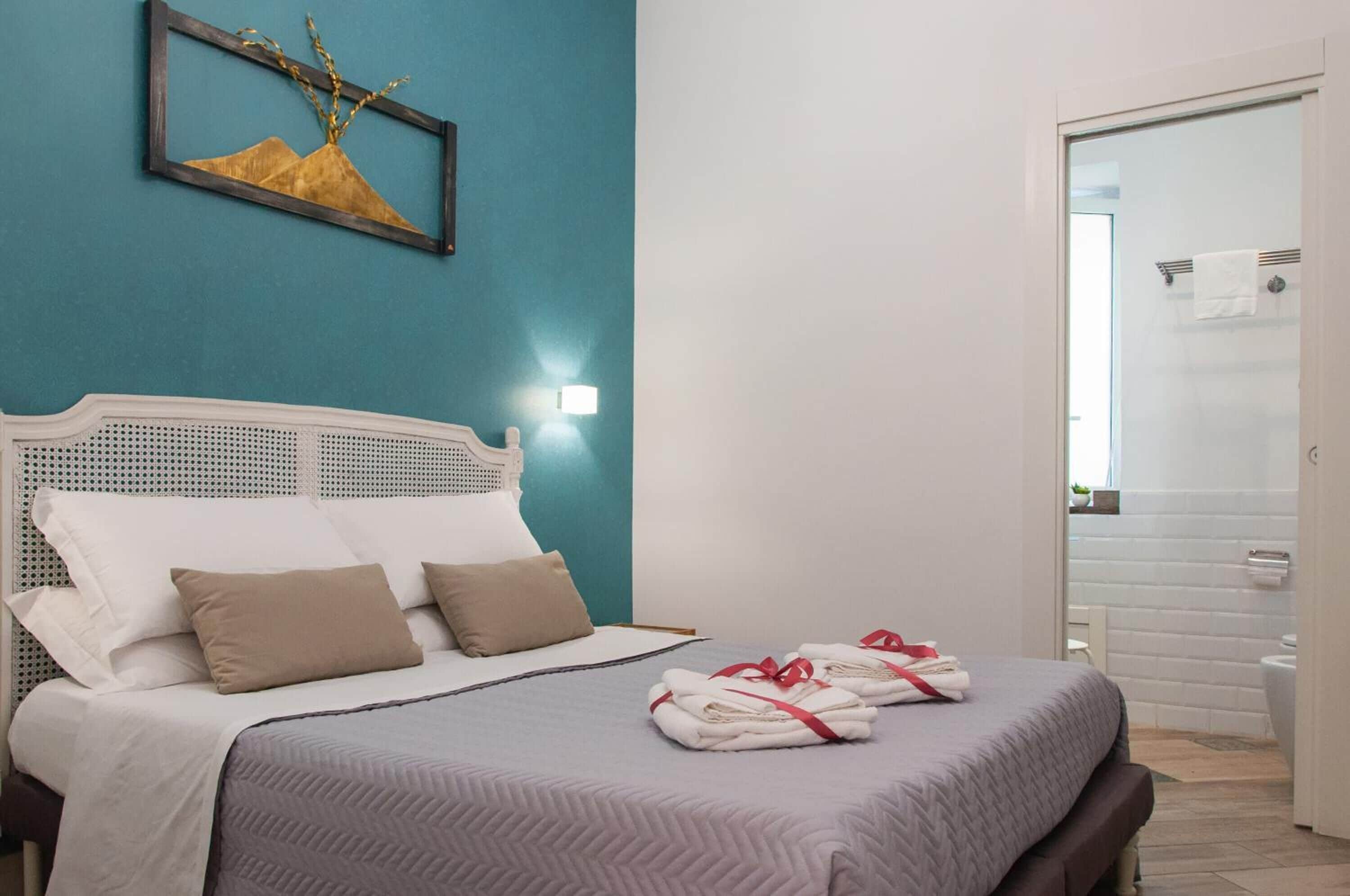 Un letto rifatto con lenzuola bianche e una coperta grigia, una testiera bianca e una lampada a parete.