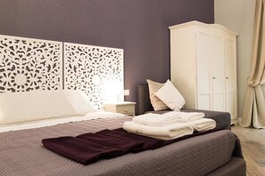 A neatly made bed with a dark headboard, a white wardrobe, and a decorative wall panel. - Real Giardinetto a Toledo (Naples)