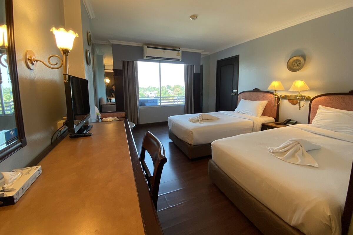 Habitación de hotel con dos camas, un escritorio con computadora, una silla y ventana con vistas al exterior.