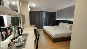 A hotel room with a bed, a desk with a kettle, a chair, and a TV.