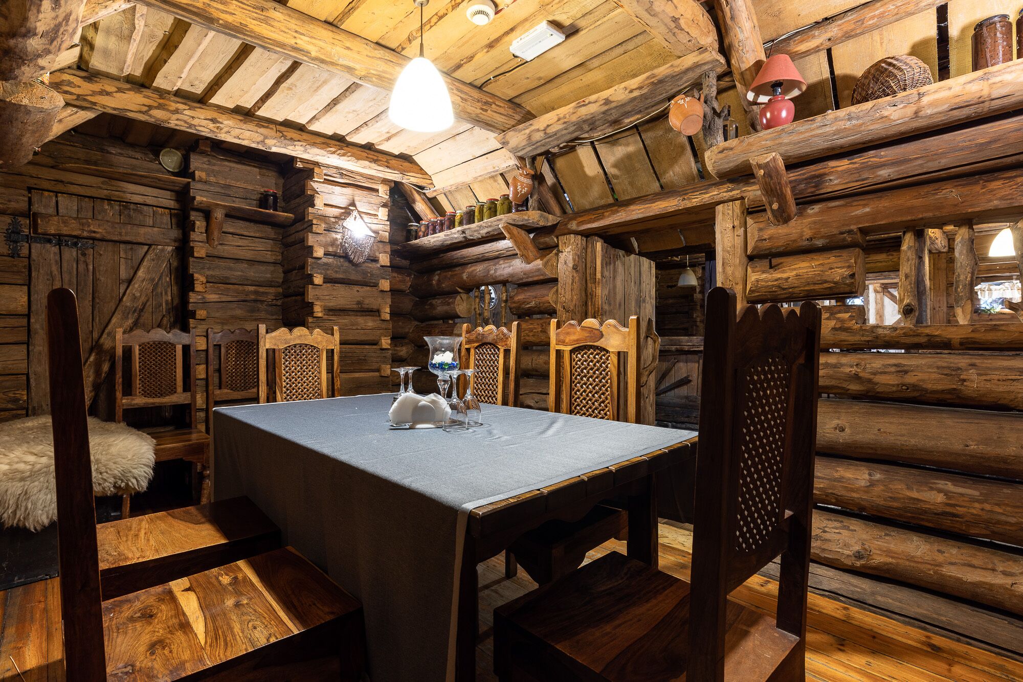 A rustic wooden cabin interior with a dining table set for two, wooden chairs, and a chandelier.