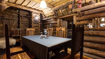 A rustic wooden cabin interior with a dining table set for two, wooden chairs, and a chandelier.