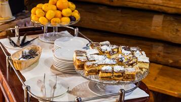 Una mesa de buffet con diversos alimentos, incluyendo un pastel en capas cubierto de azúcar glas, un tazón de naranjas y platos apilados.