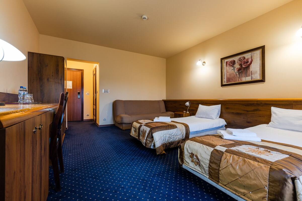 Ett hotellrum med två sängar, ett skrivbord, en stol, en garderob i trä och en tavla på väggen.
