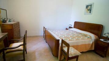 Um quarto com uma cama de madeira, uma cadeira de madeira, uma mesinha de cabeceira e um aparador.