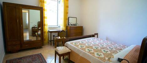 A bedroom with a bed, a desk, a chair, a wardrobe, and a window with curtains.