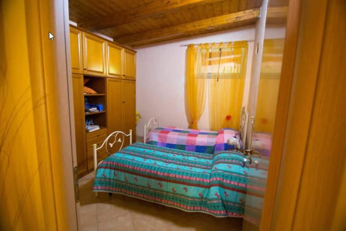 Een slaapkamer met een bed, een houten garderobe en een raam met gele gordijnen.