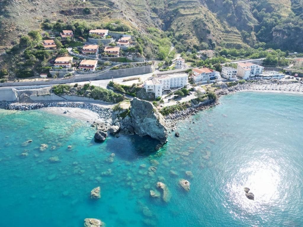 A coastal property with multiple buildings, a rocky shoreline, and clear turquoise waters.
