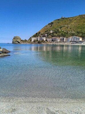 A coastal area with clear water, a rocky shoreline, and buildings on a hillside. - B&B Benvenuti al Sud (Aiello Calabro)