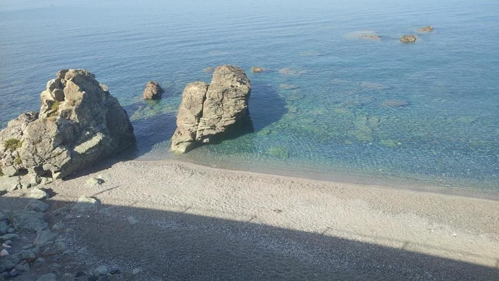 Ein Strand mit klarem Wasser, Felsformationen und einem Kiesstrand.