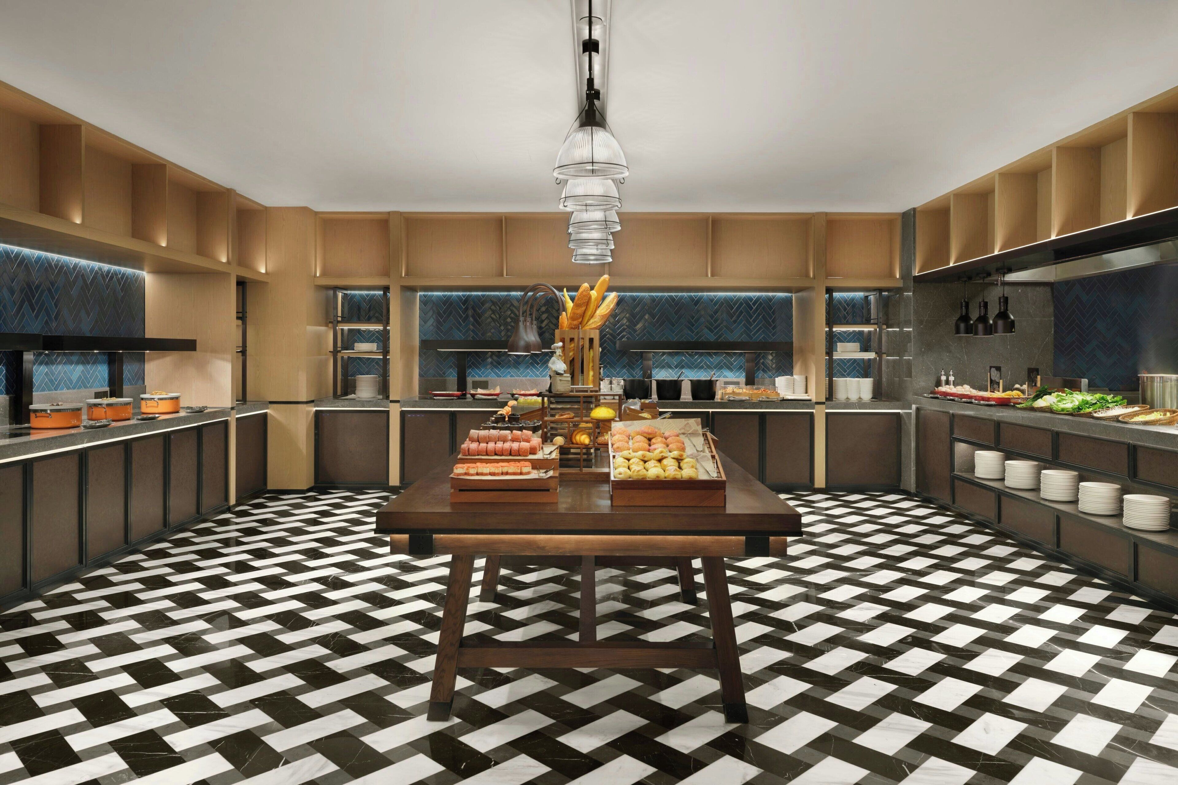 A modern kitchen with a checkered floor, a central table with food items, and built-in shelving.