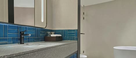 A bathroom with a grey speckled countertop, a black faucet, a white sink, a white toilet, and blue tiled walls.