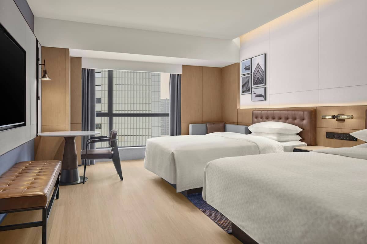 Ein Hotelzimmer mit zwei Betten, einem Schreibtisch, einem Stuhl und einem großen Fenster.