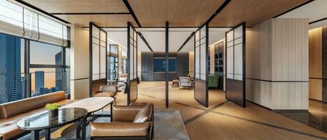A modern hotel lobby with a central seating area, a reception desk, and large windows offering city views.