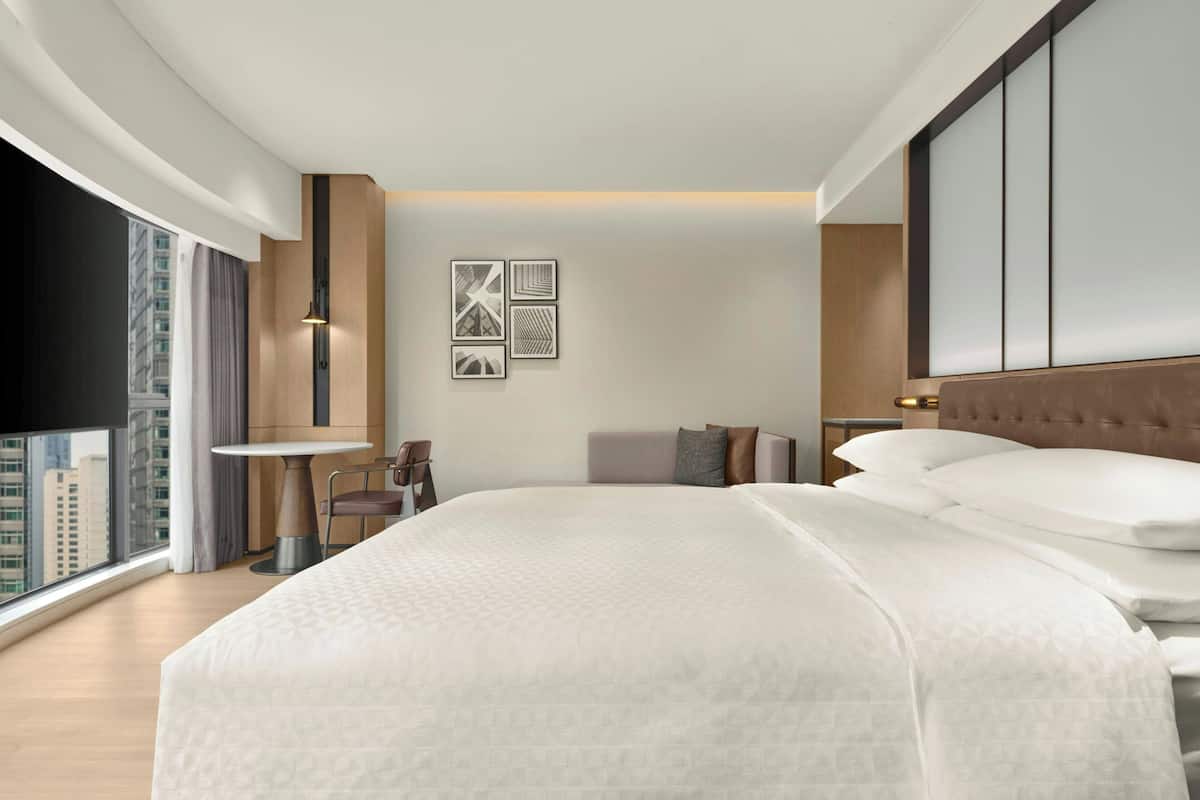 Ein modernes Hotelzimmer mit einem großen Bett, einem runden Tisch und Blick auf die Stadt.