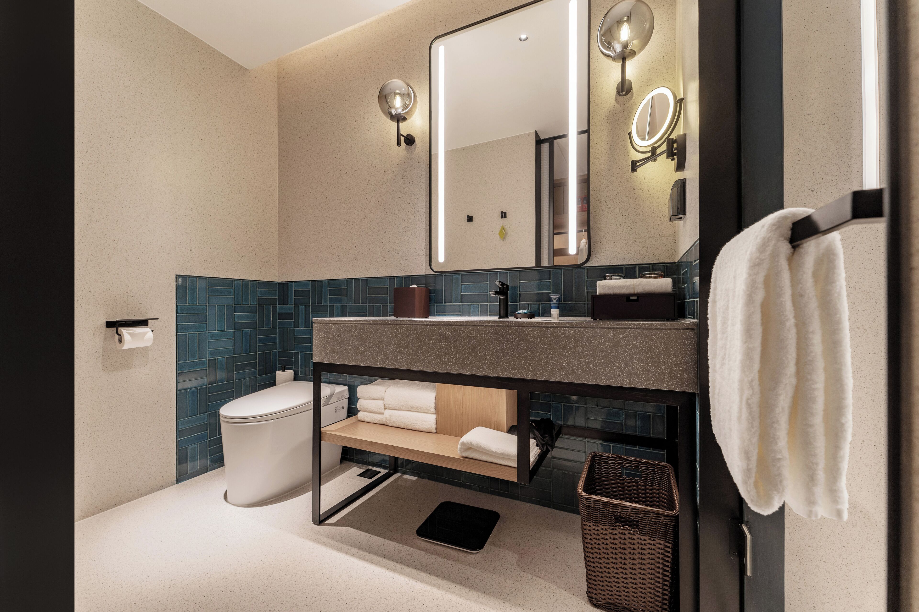 Ein modernes Badezimmer mit Toilette, Waschbecken und Spiegel. Handtücher und ein Korb stehen auf der Ablagefläche.